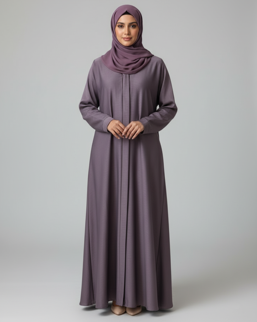 Woman wearing a long, light purple dress with a matching hijab on a plain background