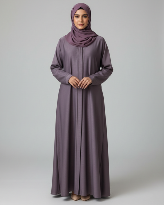 Woman wearing a long, light purple dress with a matching hijab on a plain background
