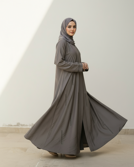 Woman wearing a long gray dress and hijab against a white background
