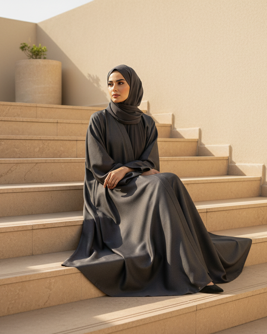 Woman in a black abaya sitting on beige steps with a neutral background