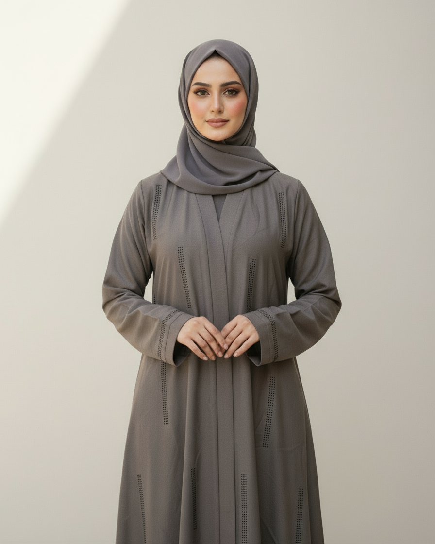 Woman wearing a gray abaya and hijab against a plain background