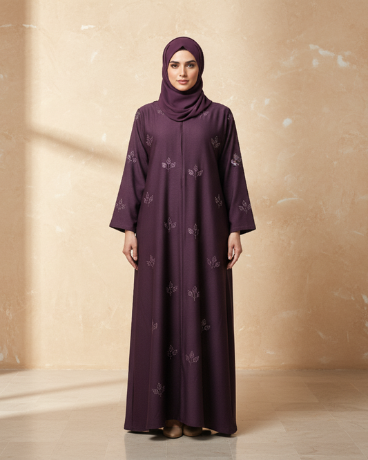 Woman wearing a purple abaya with floral patterns against a beige wall.