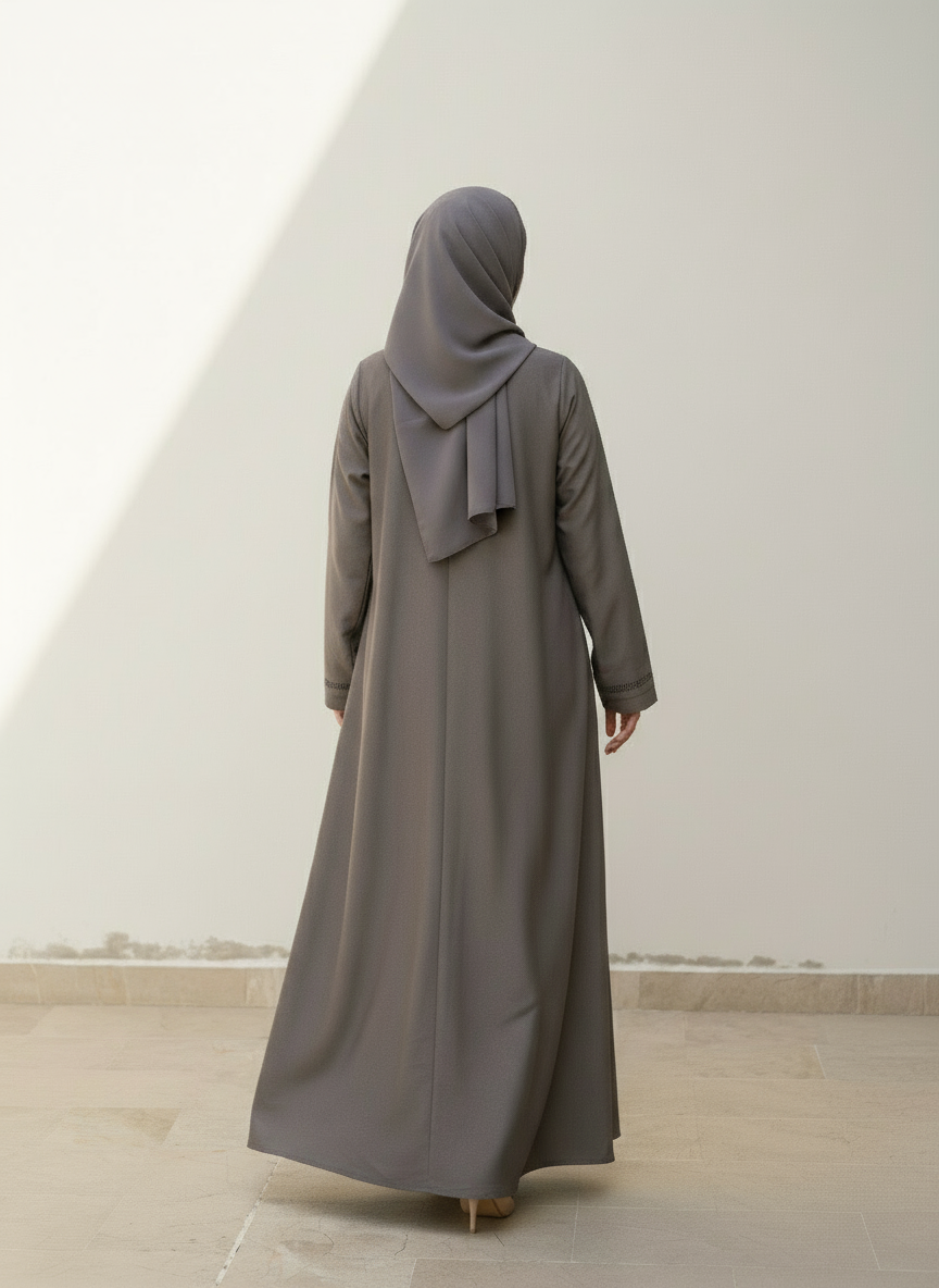 Person wearing a long, dark gray dress with a matching hijab in a minimalistic setting.