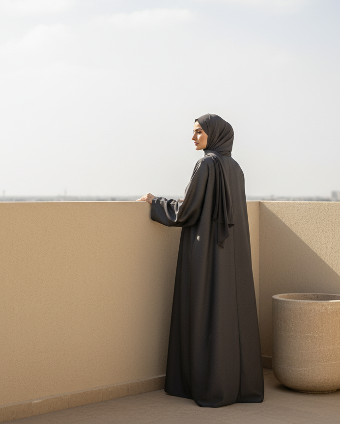 Woman in a black abaya standing on a rooftop with a plain background
