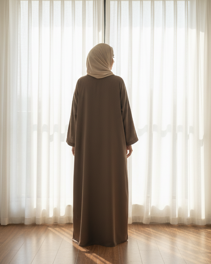 Person wearing a brown abaya standing in front of sheer curtains