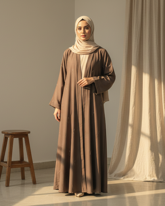 Woman in a long brown dress standing in a room with a curtain and stool.