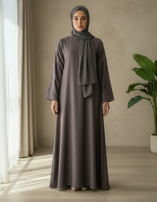 Woman wearing a long, dark brown dress and hijab standing in a well-lit room with a plant.