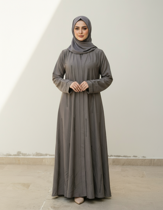 Woman wearing a long gray dress and hijab against a white wall.