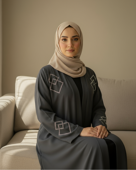 Woman wearing a hijab and dark gray dress sitting on a beige couch.