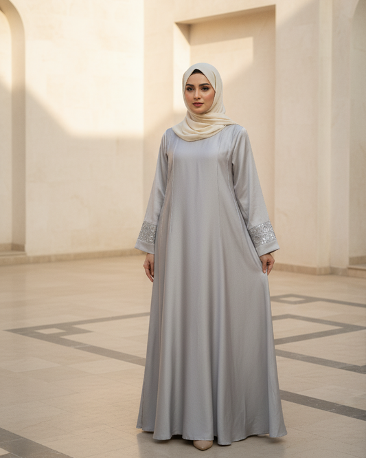 Woman wearing a light gray dress and hijab in a sunlit room with arched doorways.