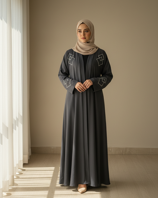 Woman wearing a long dark dress with geometric patterns in a softly lit room.