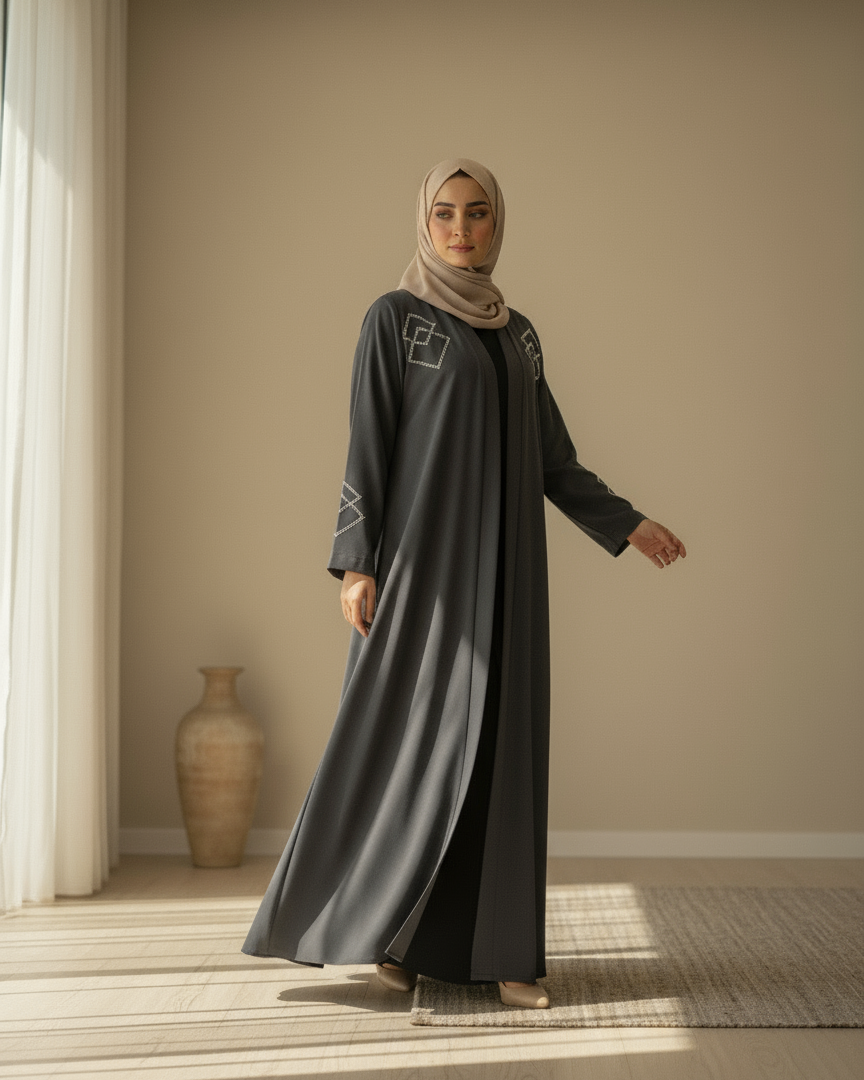 Woman wearing a long dark gray dress with a hijab in a room with a vase and light streaming in.
