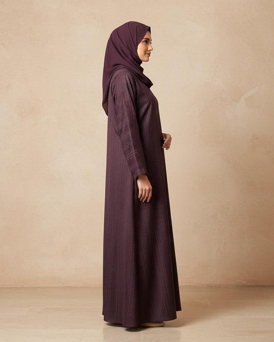 Woman wearing a long dark purple dress and hijab against a beige background
