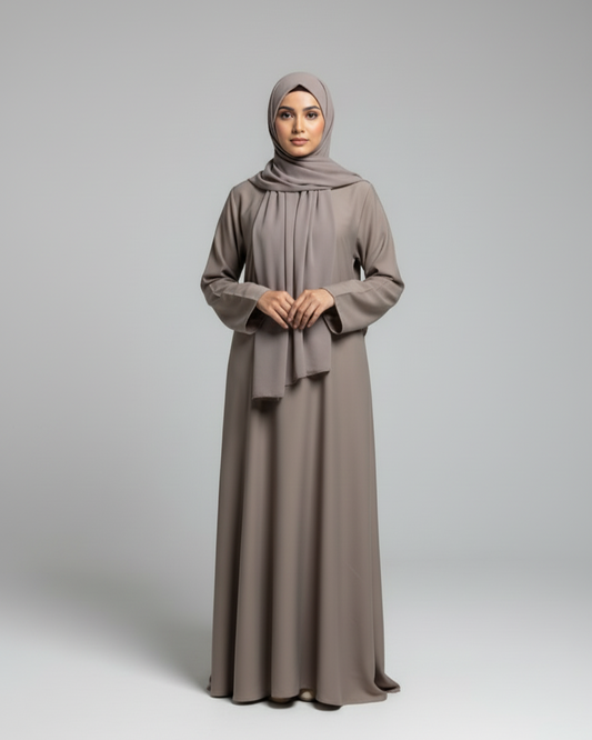 Woman wearing a long, light brown dress with a matching hijab on a gray background