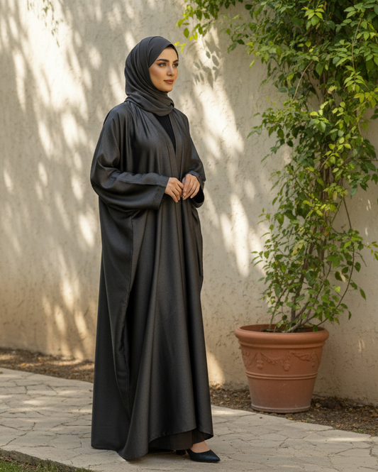 Woman in a black abaya standing outdoors against a light-colored wall with plants.